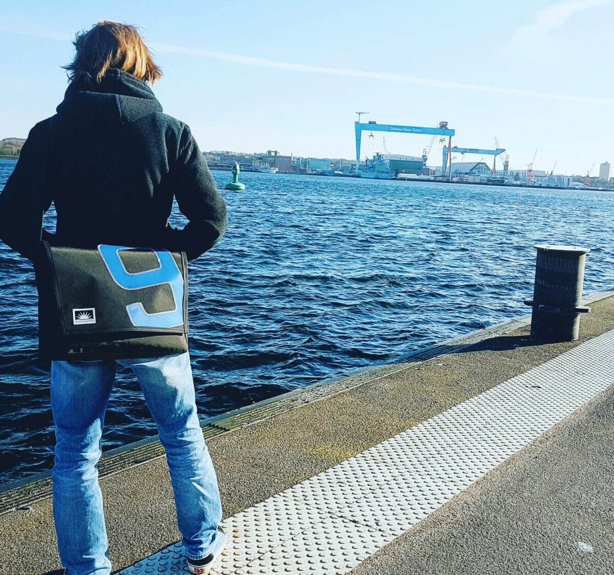 L-Quer-Tasche aus Segeltuch von Bootsmann – getragen von einem jungen Mann mit Blick auf eine maritime Hafenkulisse
