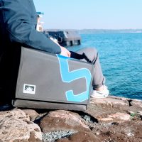 Mann sitzt am Meer, neben ihm liegt eine 17-Zoll Laptoptasche aus Segeltuch