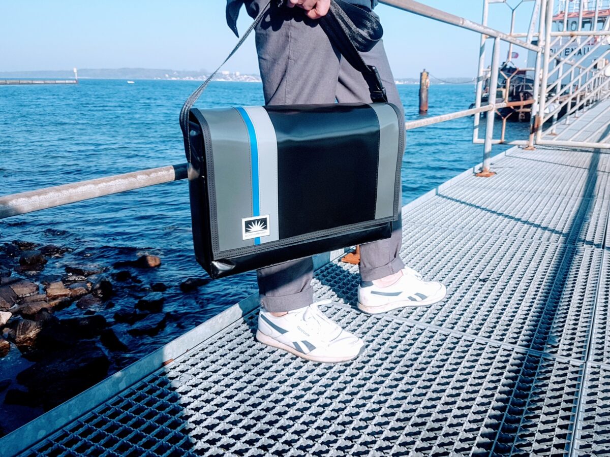 Mann steht auf Bootssteg und trägt eine Laptoptasche aus LKW-Plane