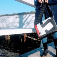 13-Zoll-Laptoptasche aus Segeltuch von Bootsmann – getragen von Frau auf Bootssteg, maritimes Design und nachhaltige Materialien