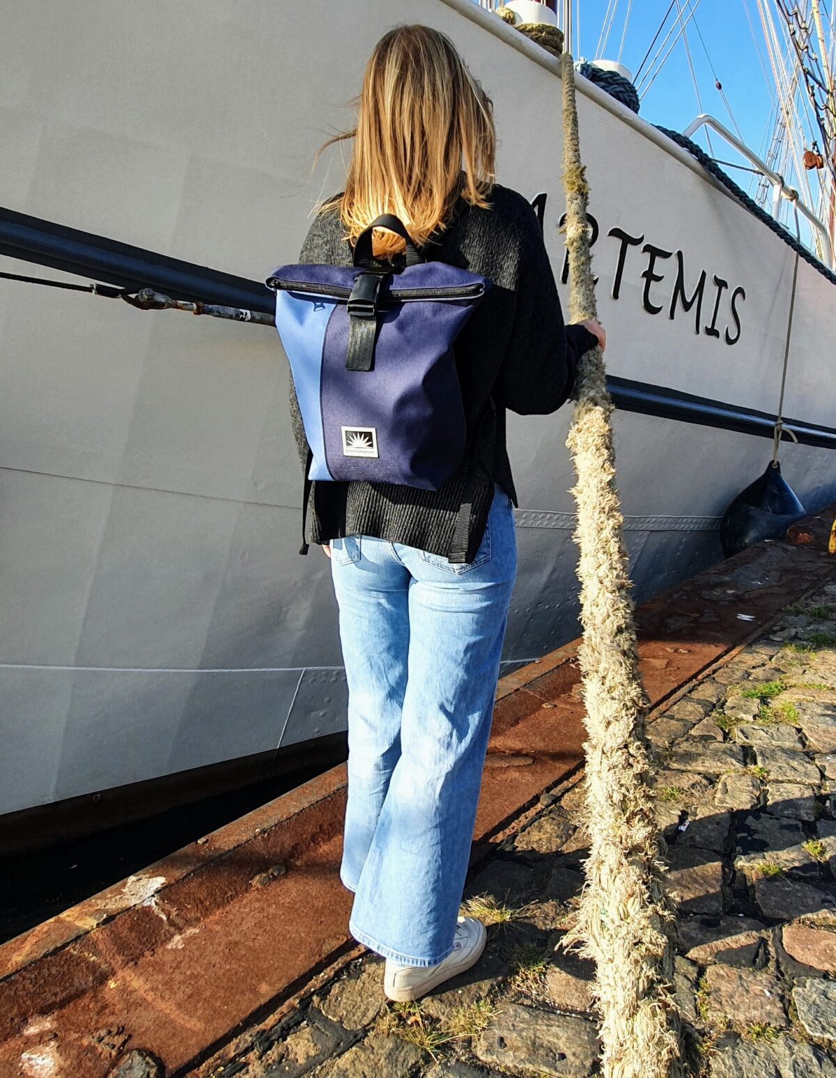 Frau steht am Kai vor einem alten Segelschiff und trägt einen BOOTSMANN-Rucksack aus Canvas in Größe S