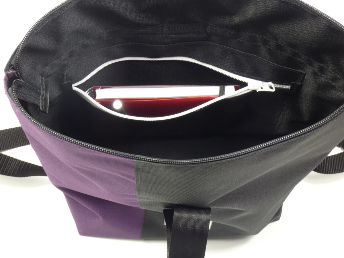Großer BOOTSMANN-Rucksack aus Canvas in Lila und Schwarz, geöffnet gezeigt, mit Blick auf die Reißverschluss-Innentasche, freigestellt