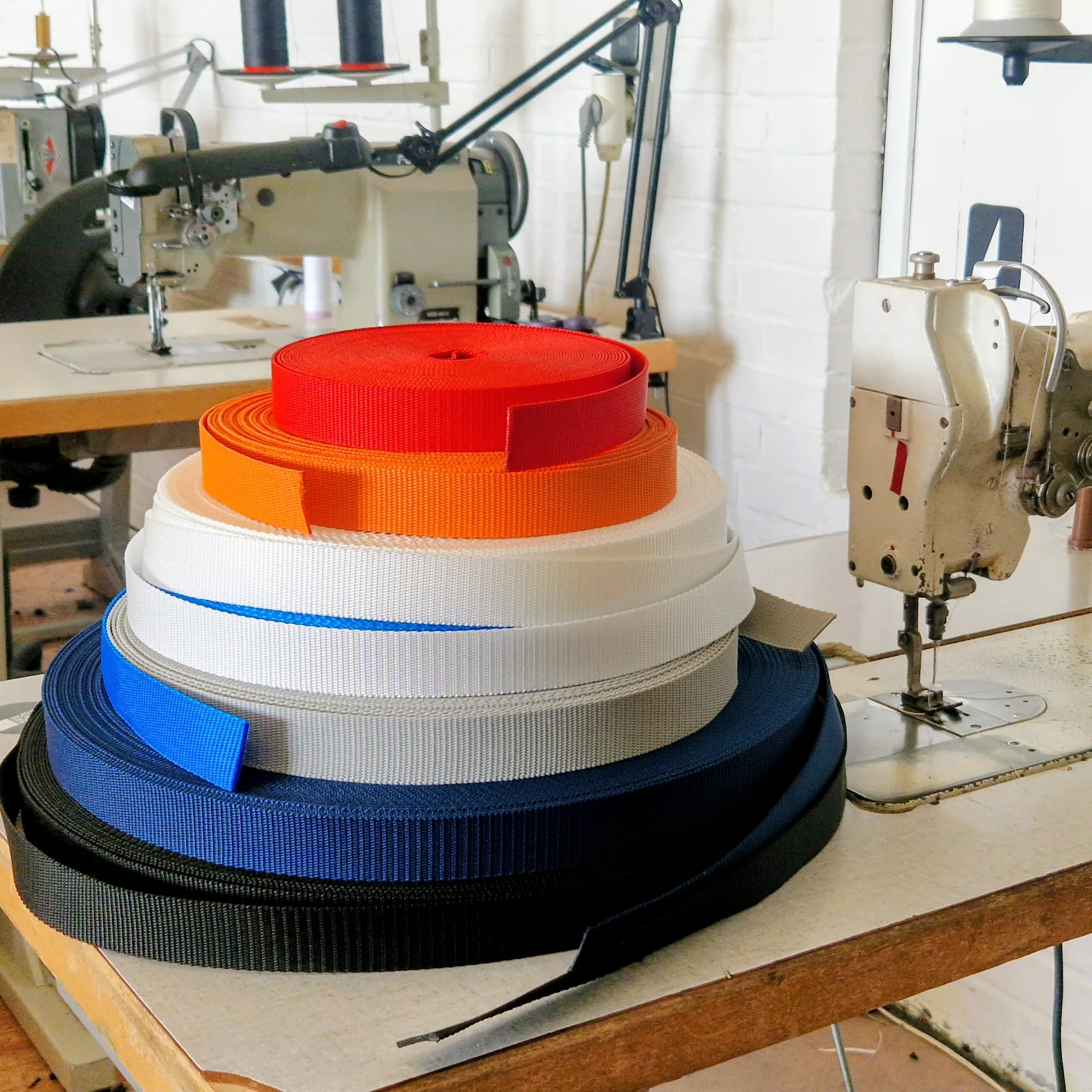 Verschiedenfarbige Gurtbandrollen liegen auf einer Nähmaschine zur Farbauswahl