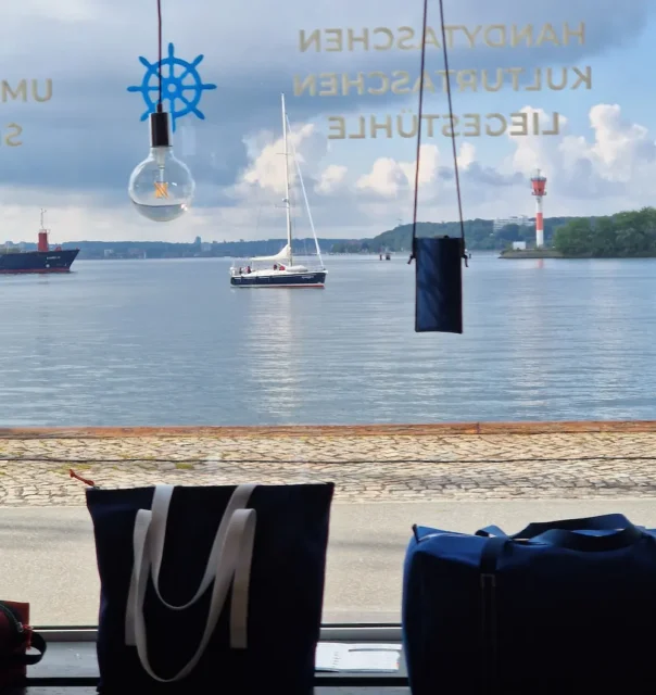 Ausblick von der Bootsmann Taschenmanufaktur am Tiessenkai auf die Kieler Innenförde mit Wasser, Booten und Uferpromenade.