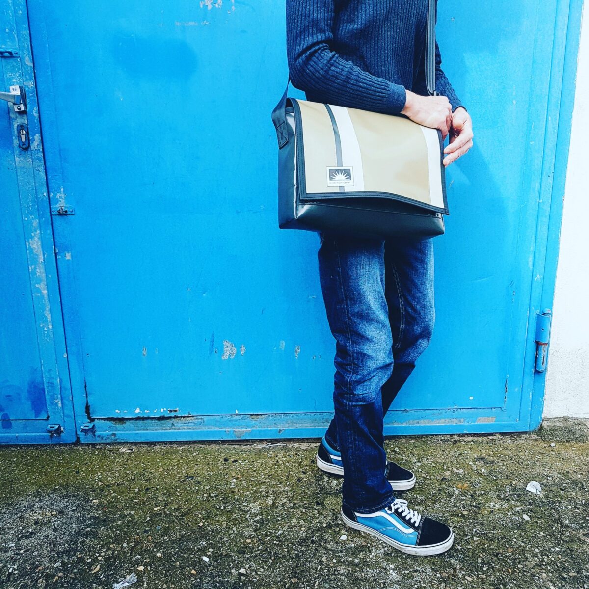 Mann steht vor Urbaner Metalltür und trägt eine Bootsmann Messenger L-quer Tasche aus LKW-Plane